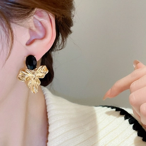Close-up of golden petal earrings with oval black crystals worn by a female model