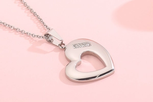 Close-up of heart-shaped stainless steel pendant with crystal accents on pink backdrop