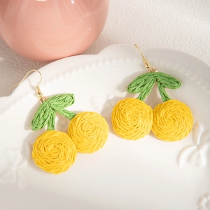 Close-up of handmade woven yellow cherry earrings with green leaves on a white ceramic plate