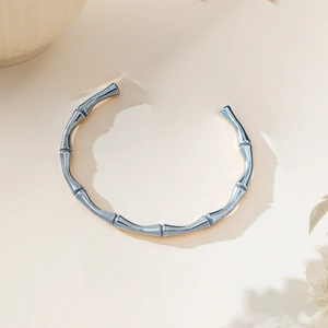 Detailed macro view of an elegant silver bamboo-style knot bangle on a beige background