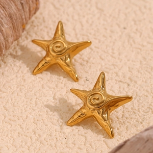 Detailed close-up of golden starfish stud earrings with unique spiral texture on sand