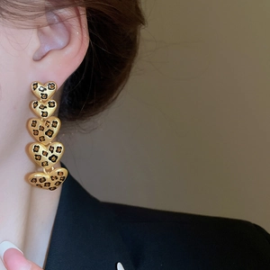 Nahaufnahme eleganter goldener Herzohrringe mit Leopardenmuster, getragen von einem Modell