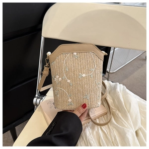 Détails de la texture tissée et broderie florale sur un sac seau en paille beige