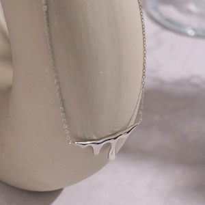 Macro shot of liquid metal drop pendant on ceramic stand in minimalist silver finish