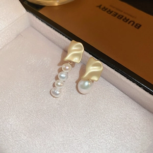 Macro shot of asymmetrical gold pearl earrings with irregular textured wave patterns