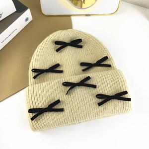 Flat lay of beige rabbit fur knit beanie with five black velvet bows on a textured background