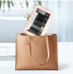 Detail showing a beige cosmetic bag being placed into a khaki leather tote with metal logo