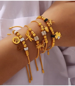 Detail of layered gold beaded bracelets featuring dragonfly, heart and clover charms