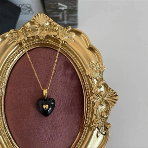 Close-up of black heart pendant with gold accent on red velvet inside vintage frame