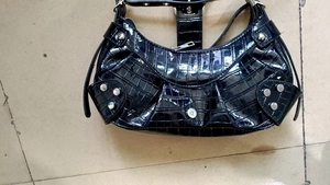 Detail of black faux crocodile patent leather bag with silver studs and zipper closure