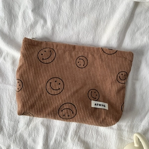 Detail of a brown corduroy bag featuring black smile patterns and a woven logo label