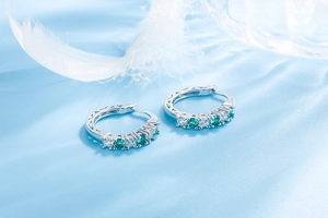 Macro detail of silver hoop earrings featuring alternating white and green crystal stones