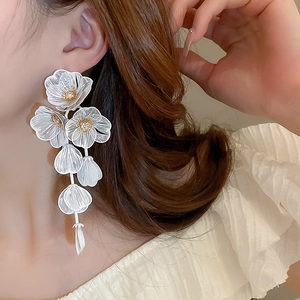 Macro detail of long floral tassel earrings with white petals and gold rhinestone core