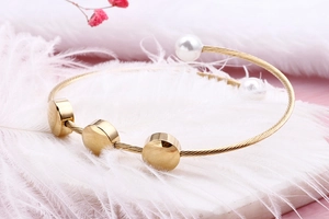 Detail of gold wire open bangle with metal charms and faux pearl ends on pink background