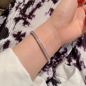 Silver tennis bracelet with square zircons worn on wrist with black patterned background