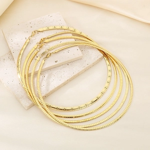 Detail of three layered gold snake bone chains with star patterns on beige silk and stone