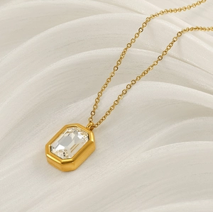Detailed view of square zircon gold pendant necklace resting on elegant white satin fabric
