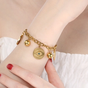 Golden stainless steel bracelet featuring evil eye and flower pendants on a model