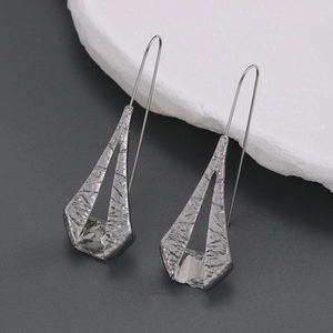 Macro shot of silver geometric earrings with irregular lava texture and metal luster