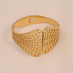 Détail du bracelet doré à motif de feuilles ajourées avec fermoir à ressort et texture métal