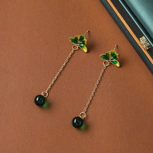 Macro shot of long gold tassel earrings with green beads and floral drip oil detail