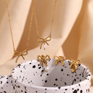 Detailed set of golden bow jewelry with white pearls and heart charms on a ceramic mug