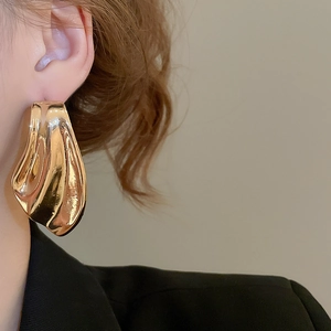 Close-up of asymmetric gold fishtail stud earrings with wavy texture on model