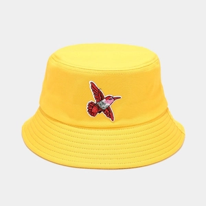 Detail of a bright yellow bucket hat featuring a colorful hummingbird embroidery and stitched brim