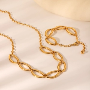 Set collana e bracciale in acciaio inossidabile dorato con maglie ovali su fondo beige