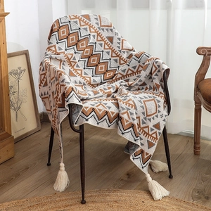 Detail of bohemian knit blanket with geometric patterns and fringe tassels on a chair