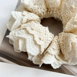 Close-up of beige layered lace and linen scrunchie with intricate floral embroidery