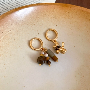 Macro detail of asymmetric tiger eye gold earrings with balloon dog charm and beads