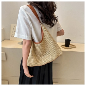 Rear view of model wearing a woven straw shoulder bag with brown leather straps