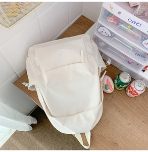 Detailansicht eines cremeweißen Nylon-Rucksacks mit Kordelzugtaschen auf einem Holztisch