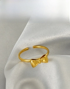 Close-up of 18k gold bow ring with brushed texture on light grey silk background