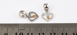 Macro view of silver heart charms with gold inlay and zircon stones next to a metric ruler