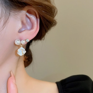 Gros plan de boucles d'oreilles fleurs avec perles blanches et bordure dorée sur modèle