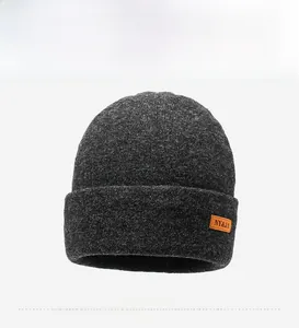 Detail showing dark grey knitted beanie with orange leather logo patch and folded brim