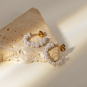 Detailed close-up of C-shaped gold pearl earrings on a textured stone display