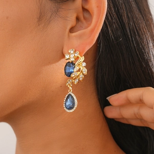 Close-up of model wearing gold drop earrings with blue water-drop stones and crystals