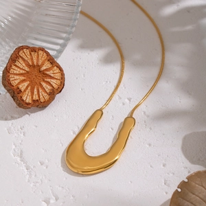 Gros plan d'un pendentif en U doré sur chaîne serpent avec ombres douces et texture