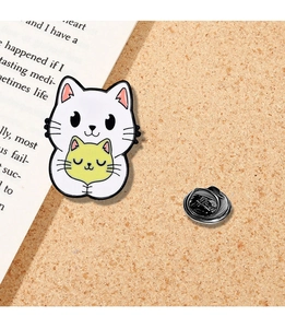 Detail of cartoon enamel pin showing a white cat hugging a yellow kitten on cork background