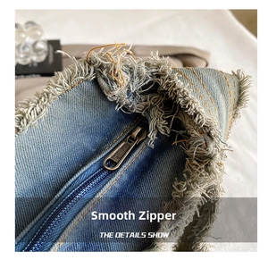 Macro shot of SBS metal zipper on washed blue denim bag with distressed frayed edges