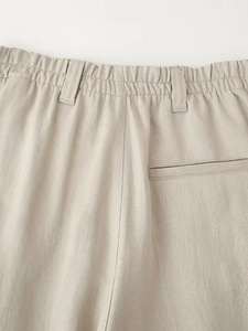 Detail of high-waisted elastic waistband and rear welt pockets on beige linen trousers