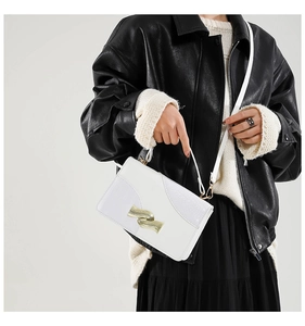 Close-up of white crossbody bag featuring crocodile pattern leather and wavy gold buckle