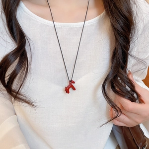 Détail d'un collier pendentif poney rouge avec cordon noir sur un pull blanc
