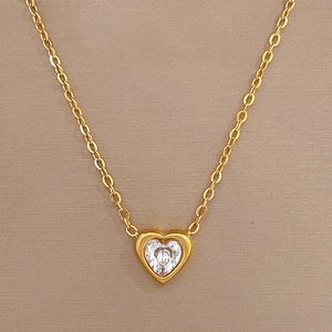 Detail of a gold heart pendant necklace featuring a central white zircon on champagne background