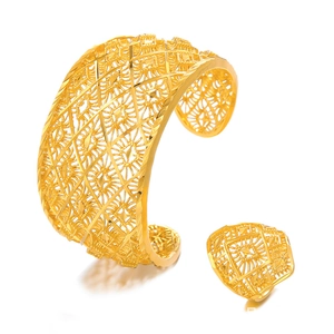 Detailed view of ornate hollow carved gold bangle and matching ring set on white background