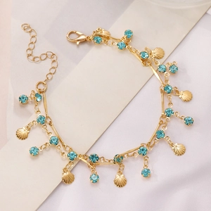 Detail of gold seashell anklet with light blue crystals on a premium satin background