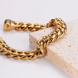 Men's bold Cuban link chain bracelet in polished gold finish on neutral stone